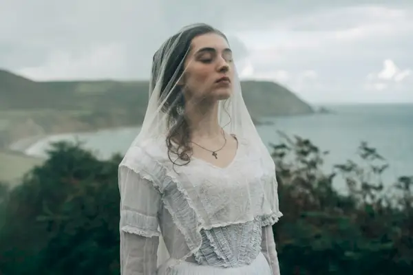 Isabelle (Anamaria Vartolomei) toda de branco, usando véu, na beira de um penhasco em