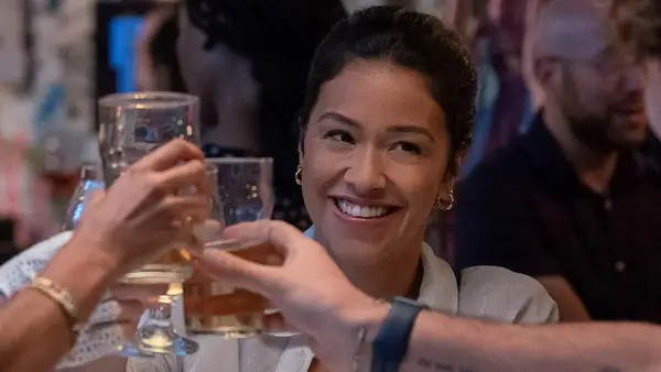 Gina Rodriguez smiles and raises a glass to cheers in a still image from Netflix