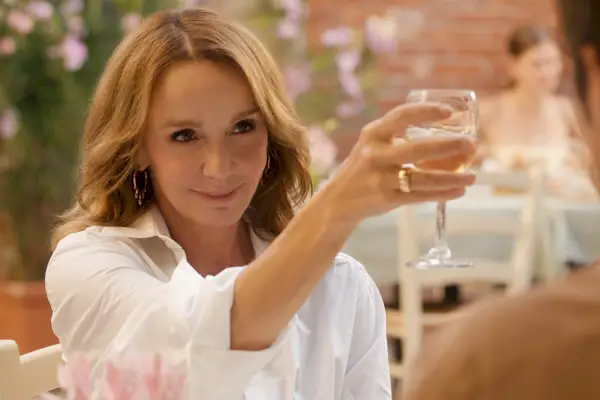 Una donna che indossa una camicia bianca, sorride e tiene in mano un bicchiere di vino