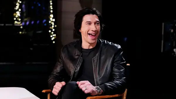 A man with light-toned skin wearing a leather jacket sitting in a director