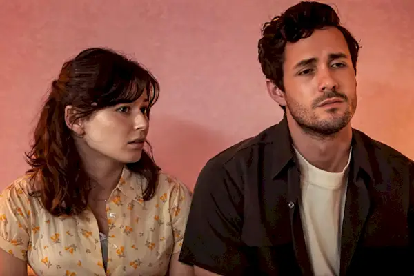 Une femme vêtue d'une chemise à fleurs regarde attentivement vers sa droite, tandis qu'un homme vêtu d'une chemise sombre et d'un t-shirt clair regarde vers l'avant.