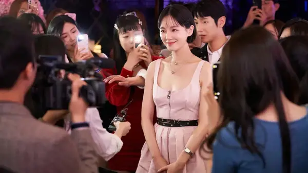 A woman in a pink dress smiles softly as people all around her take pictures of her on their phone