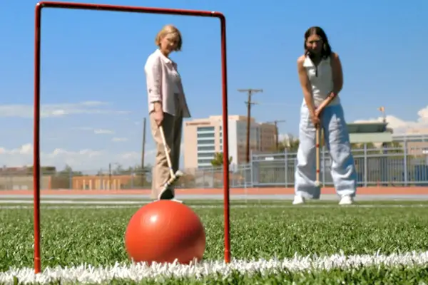 Duas mulheres jogando croquet em um campo verde.
