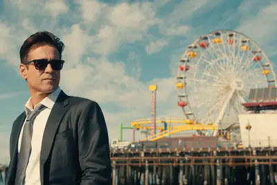 Colin Farrell in a suit standing in front of a boardwalk and Ferris wheel on 