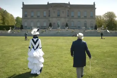 Carrie Coon and Nathan Lane in character as Bertha Russell and Ward McAllister walking towards The Elms in 