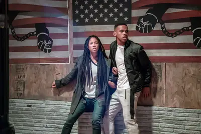 Lex Scott Davis and Joivan Wade look scared against an American flag backdrop.